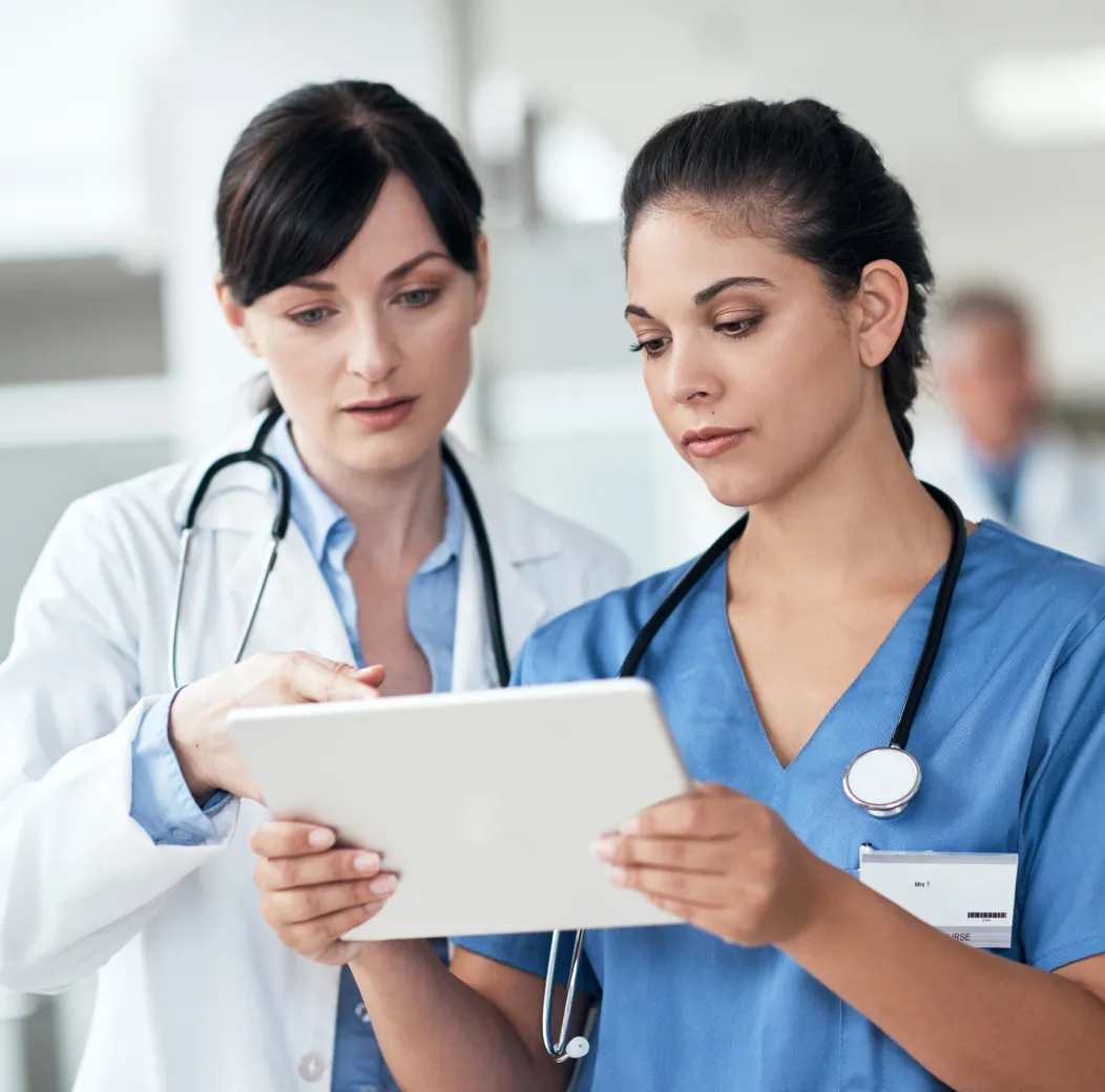 Two healthcare professionals with stethoscopes review information on a tablet.
