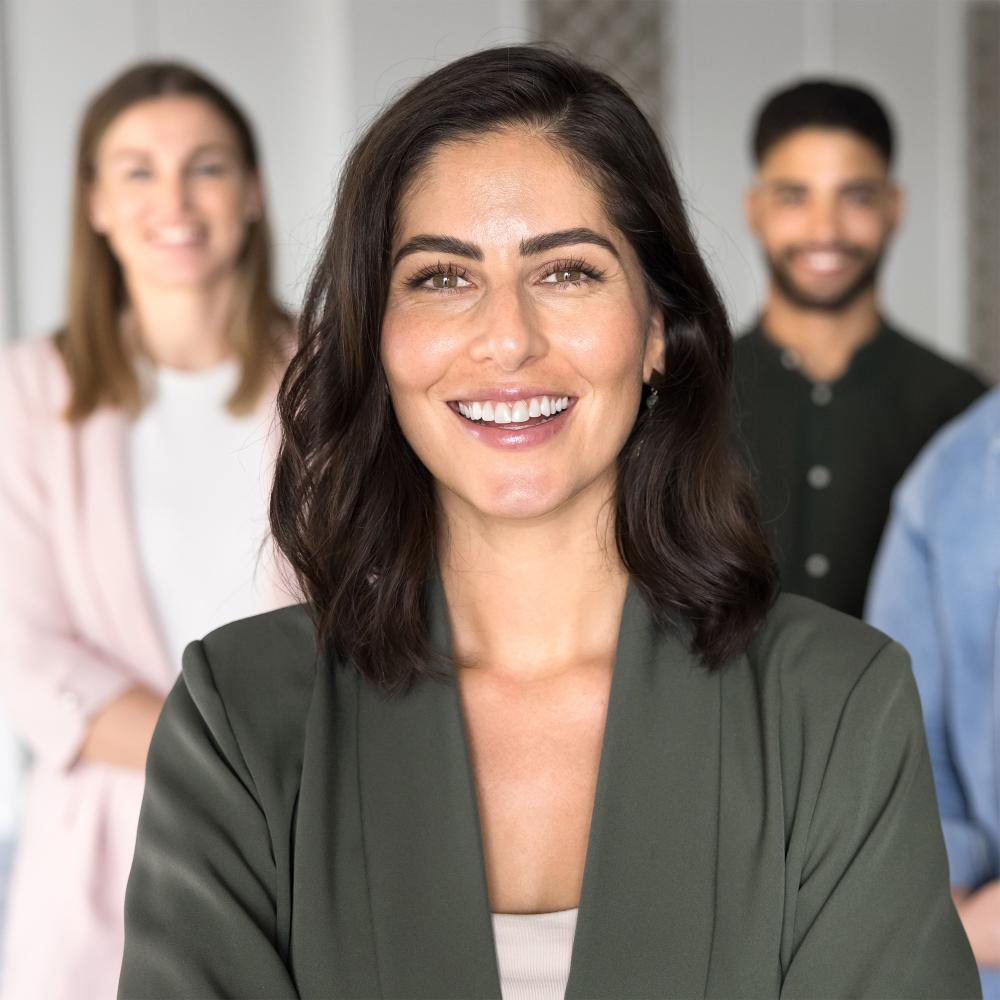 Confident professional woman smiling with a diverse group of colleagues standing behind her, representing leadership and teamwork in the field of health and human services.