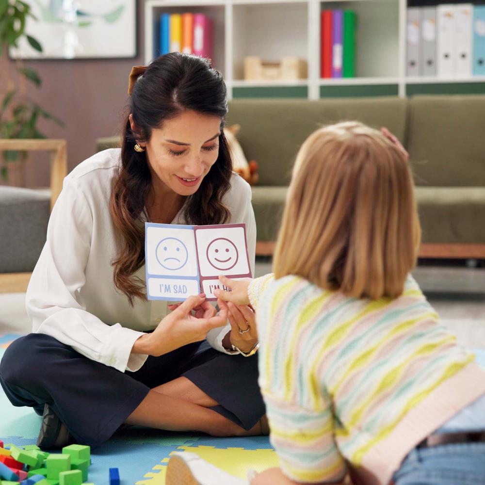 Counselor helps a child identify emotions using cards labeled I’m sad and I’m happy.