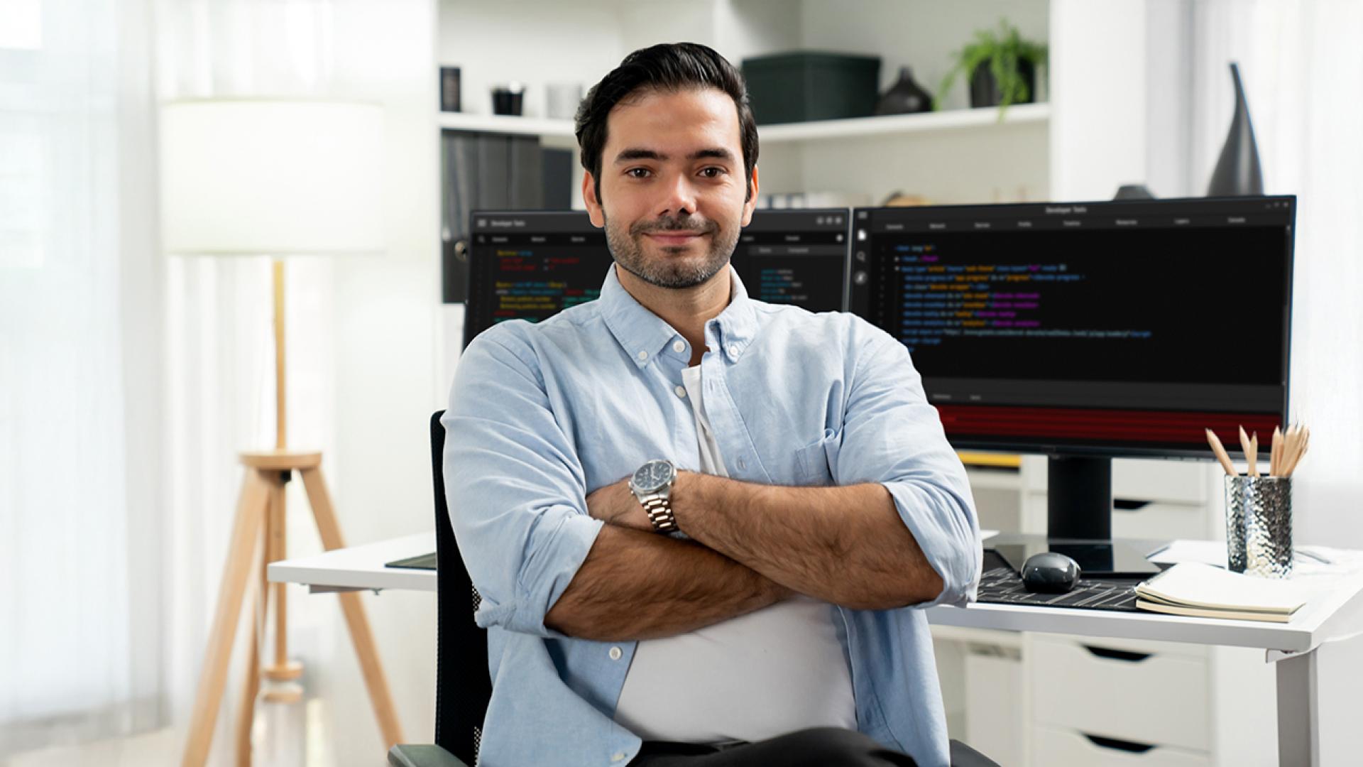 A confident professional seated in a modern office with dual monitors displaying code, representing advanced learning and career opportunities through an MS in Computer Science program.