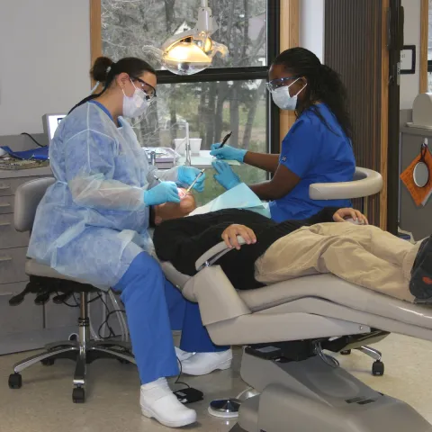 Smiling dental assistant in scrubs holding dental tools in a brightly lit dental office